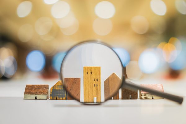 hand-holding-magnifying-glass-looking-house-model Hand holding magnifying glass and looking at house model, house selection, real estate concept.