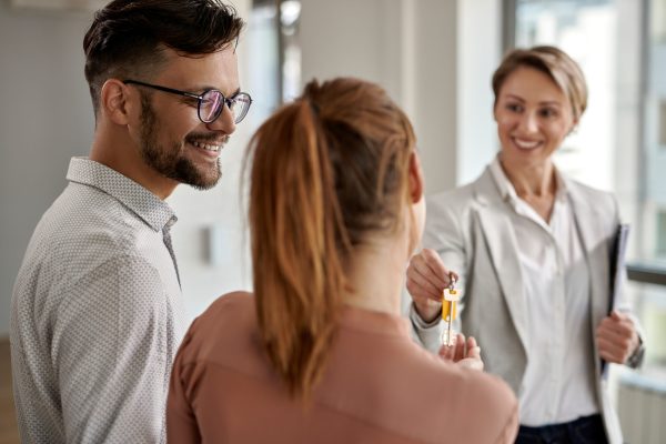 Happy couple receiving new house keys from real estate agent. Young happy couple buying a new home and receiving key from their real estate agent.